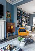 Blue built-in shelving unit, elegant highboard and yellow armchair in a living room