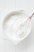 White meringue mixture beaten on white bowl with whisk