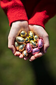 A child holds many small shiny easter eggs in his cupped hands.