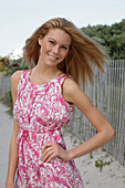 Blonde Frau in rosa-weißem Sommerkleid am Strand