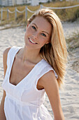 Blonde Frau in weißem Sommerkleid am Strand