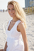 Blonde Frau in weißem Sommerkleid am Strand