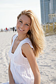 Blonde Frau in weißem Sommerkleid am Strand