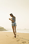 Young Woman Listening To Music With Her Headphones On The Beach; Xiamen, China