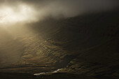 Das Sonnenlicht scheint durch die Sturmwolken und erhellt die Hänge der isländischen Ostfjordregion; Island