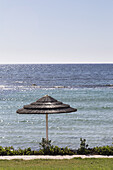 Ein strohgedeckter Regenschirm steht am Wasser; Paphos, Zypern