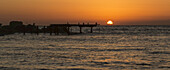 Die goldene Sonne versinkt hinter dem Wasser bei Sonnenuntergang mit orangefarbenem Himmel; Paphos, Zypern