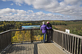 Mature Couple Overlooking Sunday Creek From The Algonquin Park Visitor Centre Observation Deck On A Sunny Afternoon In Autumn; Ontario, Canada