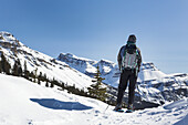 Schneeschuhwanderin mit Blick auf eine schneebedeckte Bergkette und blauen Himmel; Banff, Alberta, Kanada