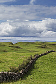 Eine Steinmauer, die sich über Grasfelder erstreckt, mit Blick auf den Ozean