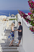 Ein Paar steht auf einem Gehweg an einer weiß getünchten Mauer auf einer griechischen Insel; Santorini, Griechenland