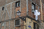 Ecke eines Backsteingebäudes mit einer an der Wand befestigten Lampe und aus einem Fenster hängenden Stoffen; San Sebastian, Spanien