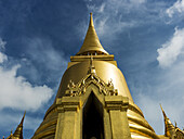 Goldene Struktur mit Turmspitze vor blauem Himmel und Wolken, Tempel des Smaragdbuddhas (Wat Phra Kaew); Bangkok, Thailand