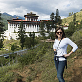 Eine Frau posiert mit dem Rinpung Dzong im Hintergrund; Paro, Bhutan