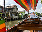Ein Boot auf dem Fluss mit einer bunten Decke und Häusern entlang der Uferlinie; Bangkok, Thailand