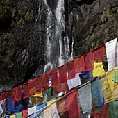 Colourful Prayer Flags And A Waterfall Down A Cliff In The Background; Paro, Bhutan