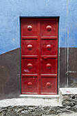 Rote Metalltür an einer braun und blau gestrichenen Wand; San Miguel De Allende, Guanajuato, Mexiko