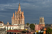 Kirche und Stadtbild unter bewölktem Himmel, mit einem Heißluftballon in der Ferne; San Miguel De Allende, Guanajuato, Mexiko