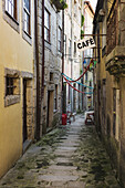 Grünes Moos auf dem Stein einer schmalen Gasse zwischen Gebäuden und einem Café-Schild; Porto, Portugal
