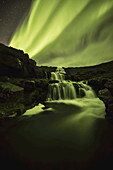 Nordlicht, oder Aurora Borealis, leuchtet über Wasserfälle und einen Strom; Island