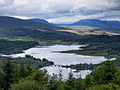 Flusslandschaft und Wälder über Bergen bei bewölktem Himmel; Schottland