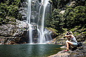 A Young Woman Photographs The Cunca Rami Waterfall; Flores, Indonesia