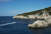 Ein Boot nähert sich der zerklüfteten Küstenlinie der Insel Capri; Anacapri, Capri, Kampanien, Italien