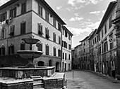 Eine leere Straße zwischen zwei Wohngebäuden und einem Wasserbrunnen im Vordergrund; Siena, Italien