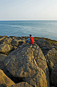 Wanderer sitzt auf einem Felsen mit Blick auf die Küstenlinie, Bay Of Fundy; Long Island, Nova Scotia, Kanada