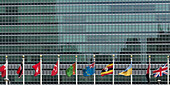 Internationale Flaggen in einer Reihe vor dem Hauptsitz der Vereinten Nationen mit Glasfassade; New York City, New York, Vereinigte Staaten von Amerika