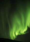 Man Standing Under A Bright Display Of The Northern Lights; Iceland