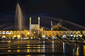 Lichter, die Wasserfontänen und ein Gebäude bei Nacht beleuchten; Isfahan, Iran