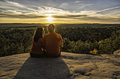 Paar, das auf einer Klippe sitzt und die Herbstfarben im Algonquin Park bei Sonnenuntergang betrachtet; Ontario, Kanada