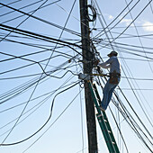 Electrician repairing power line cables on a post,French Harbour; Roatan, Bay Islands Department, Honduras