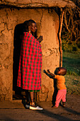 Frau in Shuka mit Kind vor Hütte; Tansania