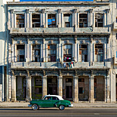 An old car passes the weathered facade of old buildings along a street; Havana, Cuba
