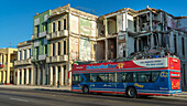 A tour bus passes the weathered facade of old buildings along a street; Havana, Cuba