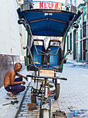 A man repairs his cycle rickshaw on the side of the street; Havana, Cuba