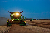 A combine with its lights on harvesting canola after sunset; Legal, Alberta, Canada