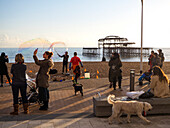 Making soap bubbles on the beach promenade with people and dogs watching and West Pier in background; Brighton, East Sussex, England