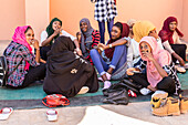 Young Sudanese women sitting on the ground visiting and eating together; Kerma, Northern State, Sudan