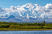 The mountain Denali in Denali National Park and Preserve, viewed from the Park Road driving to Wonder Lake. Photo shows hikers in back of Reflection Pond and dwarfed by Denali; Alaska, United States of America