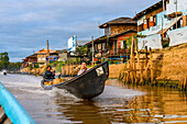 Boat with two passengers in the river along the shoreline; Yawngshwe, Shan State, Myanmar