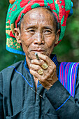 Burmese woman wearing a traditional head covering and smoking a cigarette; Yawngshwe, Shan State, Myanmar