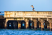 A boy jumps off the wharf into Hana Bay; Maui, Hawaii, United States of America