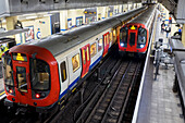 Tube Station mit Zügen auf den Gleisen und wartenden Fahrgästen auf dem Bahnsteig; London, England
