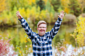 A young man with Down Syndrome raising his hands in worship to God, while in a city park on a warm fall evening: Edmonton, Alberta, Canada