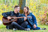 A mature couple spending quality time together and the wife is listening to her husband singing and playing his guitar while in a city park on a warm fall evening: Edmonton, Alberta, Canada