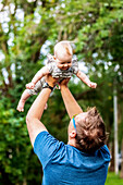 A father holding his baby girl in the air while outdoors during the fall; Edmonton, Alberta, Canada