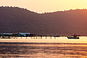 Boote und Gebäude auf dem Wasser während eines leuchtend rosa Sonnenuntergangs, Starfish Beach; Phu Quoc, Provinz Kien Giang, Vietnam